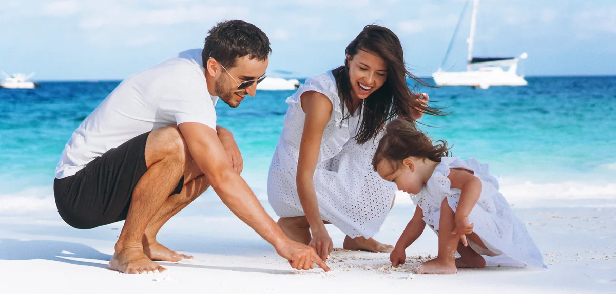 Imagen IUL Para Ninos - Familia joven con pequeña hija en la playa en el fondo un yate flotando en el agua