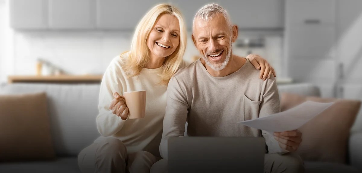 Matrimonio Adulto sonriendo viendo la pantalla de una laptop disfrutando de su Jubilación a través de una IUL